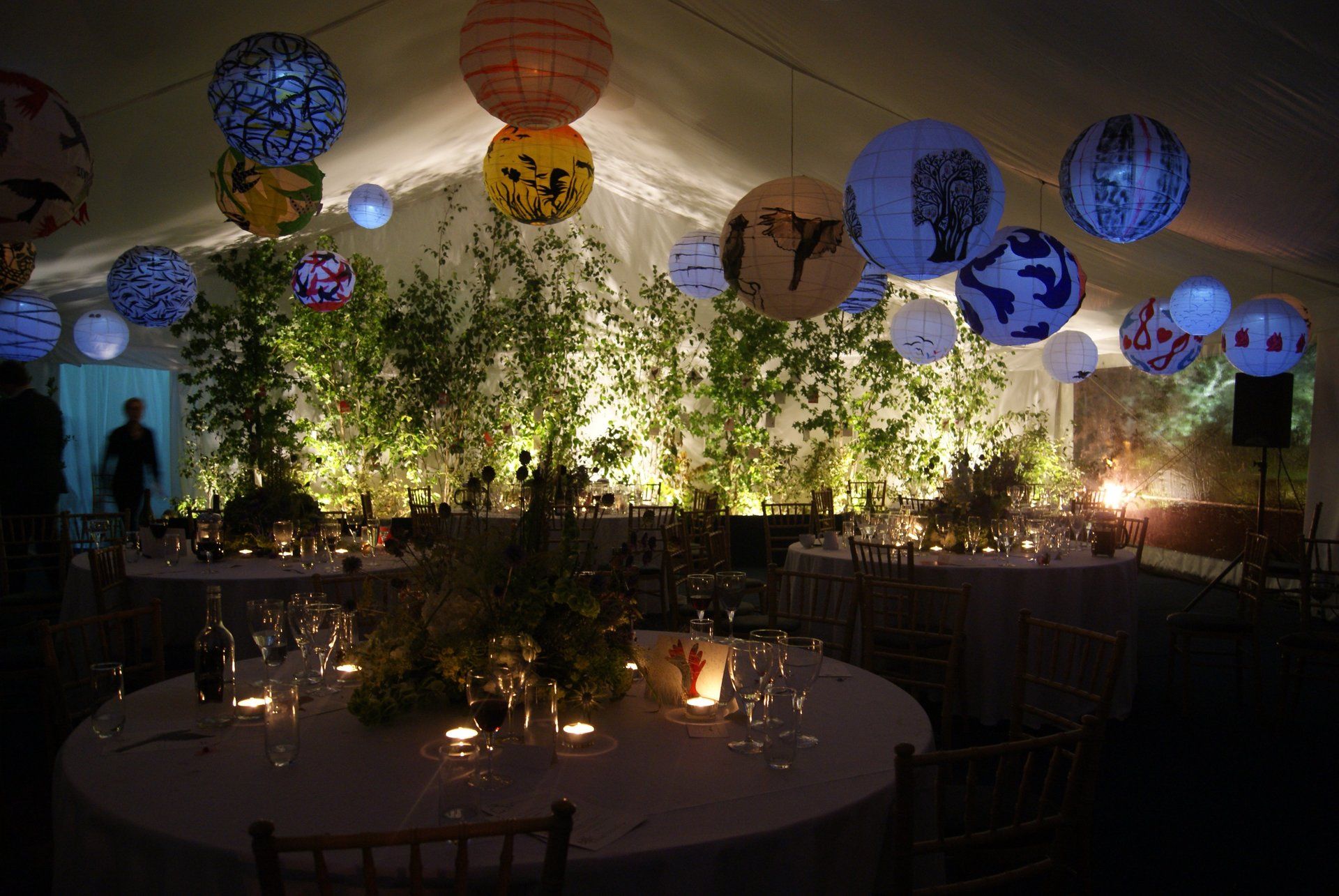Decorated indoor event hall with glowing lanterns, string lights, and round tables set for a reception