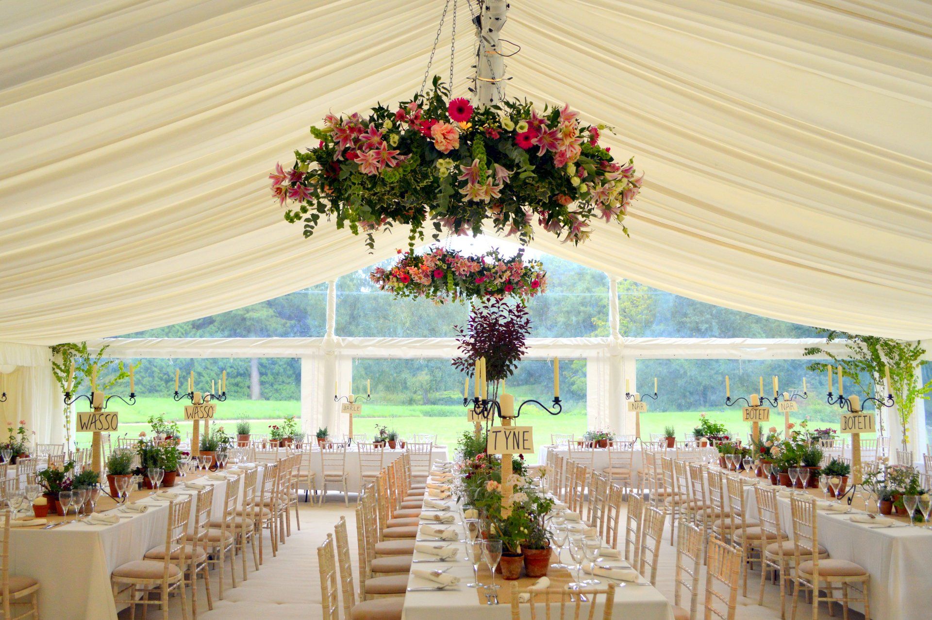 Elegant wedding reception tent with white drapes, floral chandeliers, and rows of tables and chairs