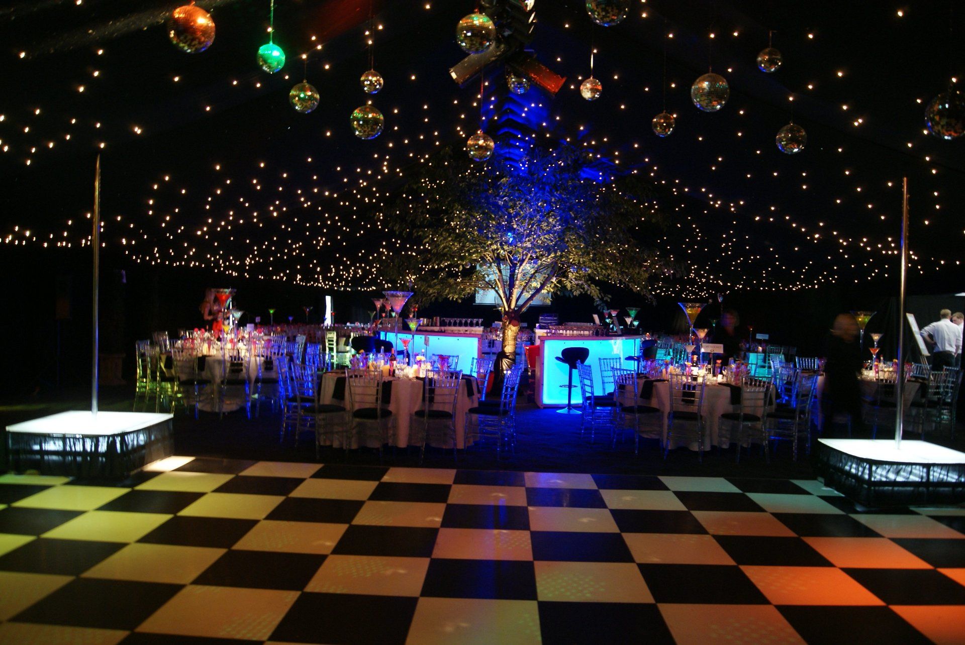 Dimly lit banquet hall with checkered dance floor, glowing ceiling lights, and decorated tables and chairs