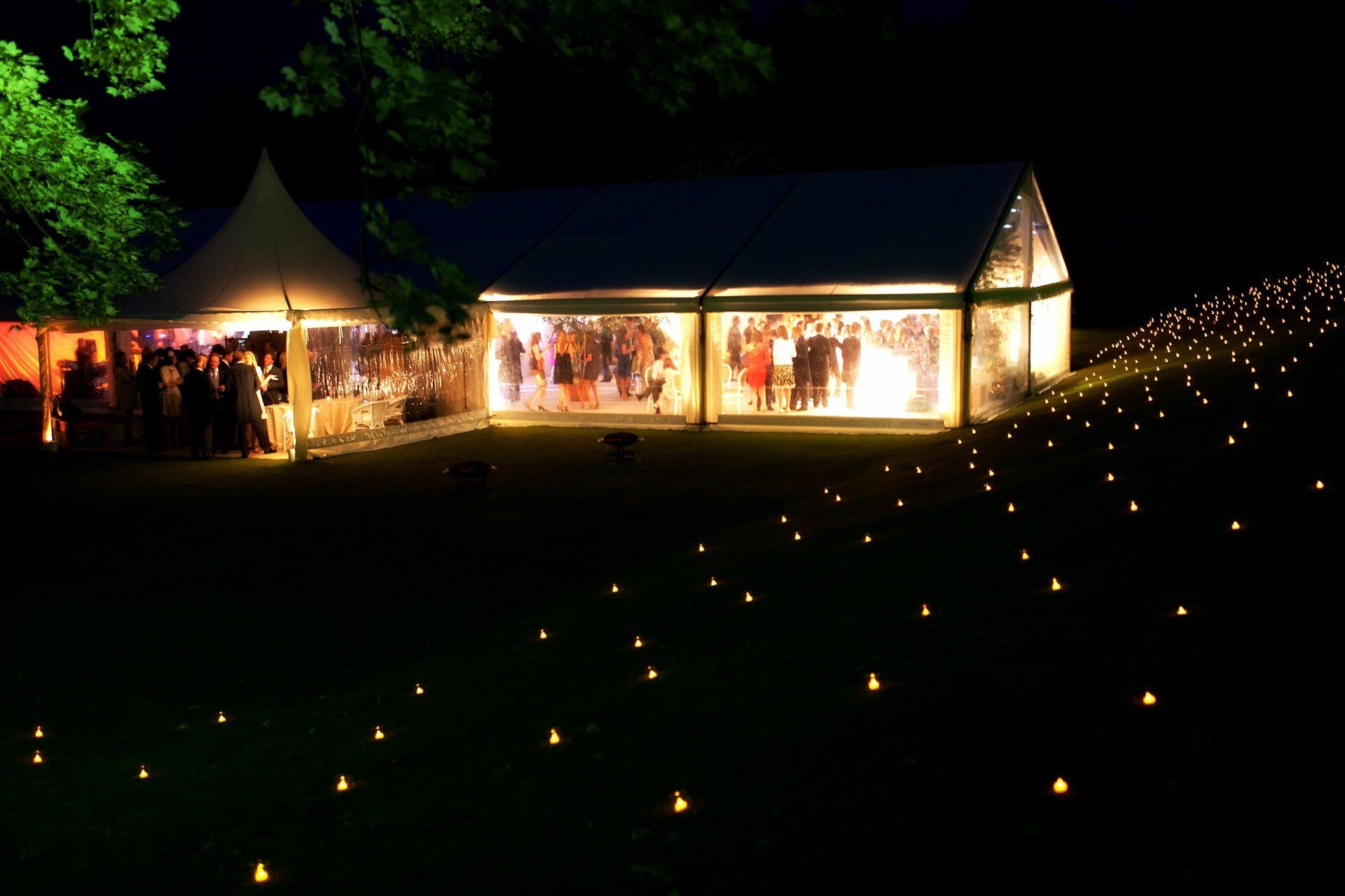 Illuminated outdoor event tents at night with warm lights and pathways marked by small lanterns