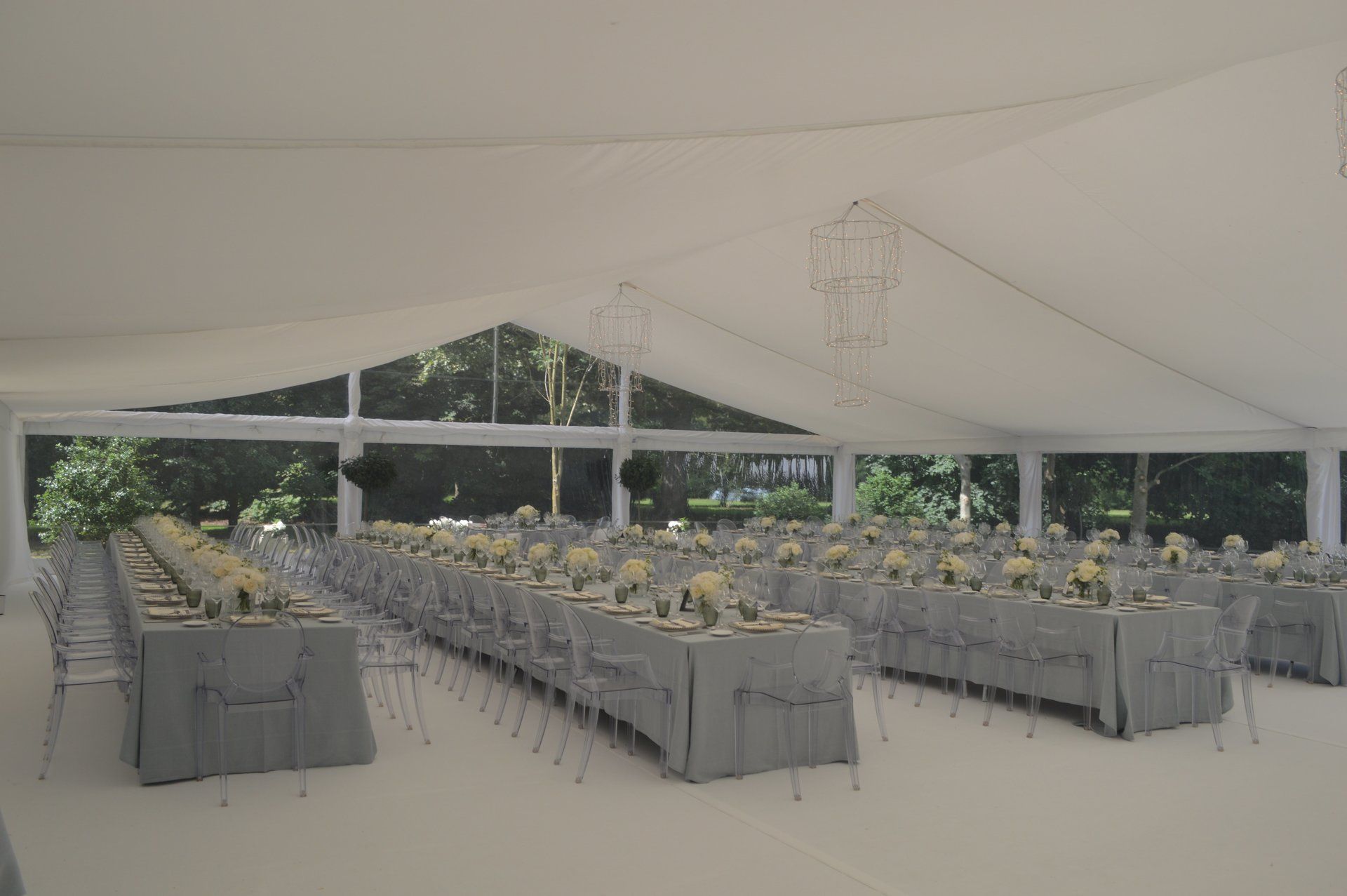 White wedding tent set for a reception with long gray tables, chairs, and floral centerpieces.