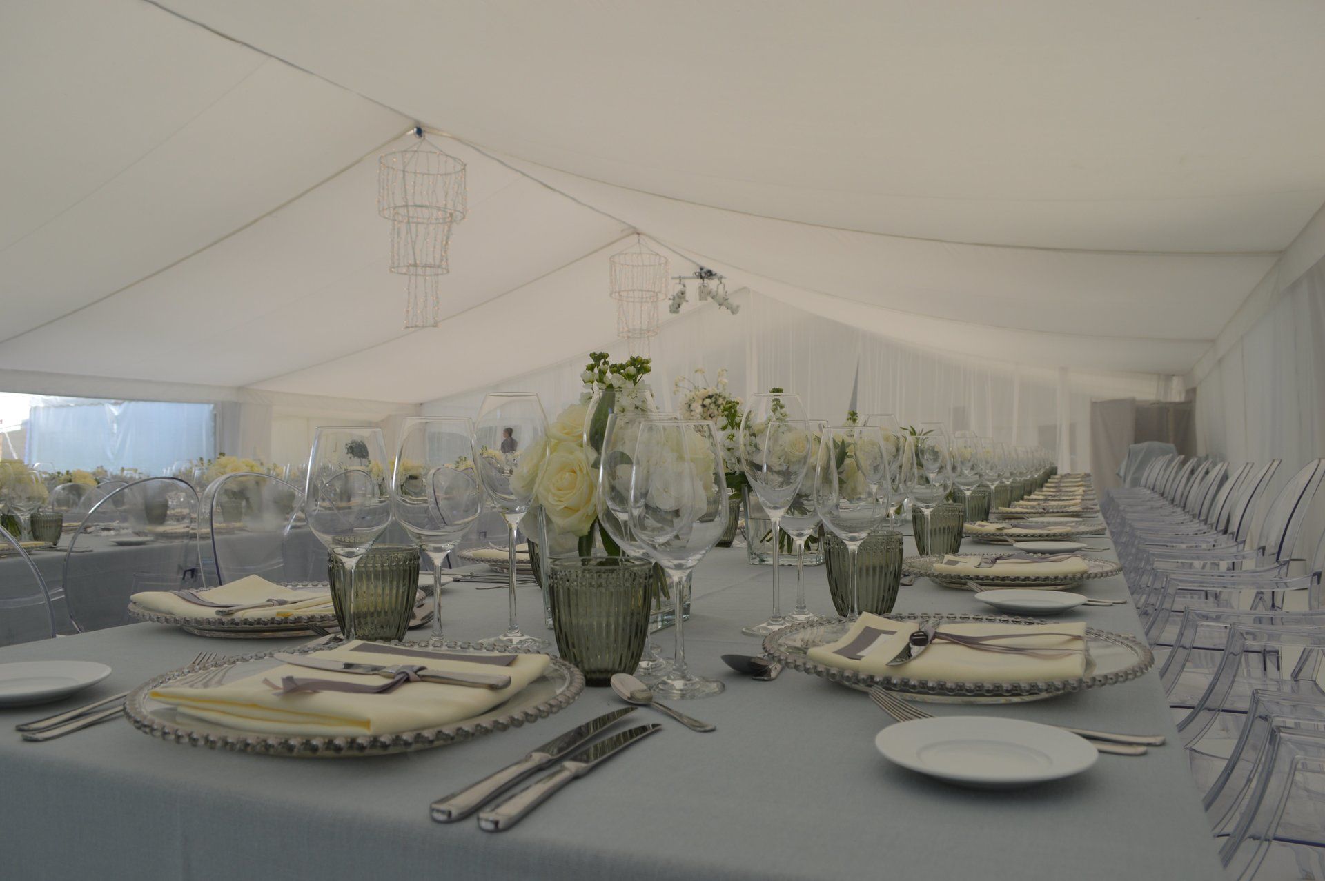 Elegant outdoor dining tent set with long tables, white chairs, and floral centerpieces