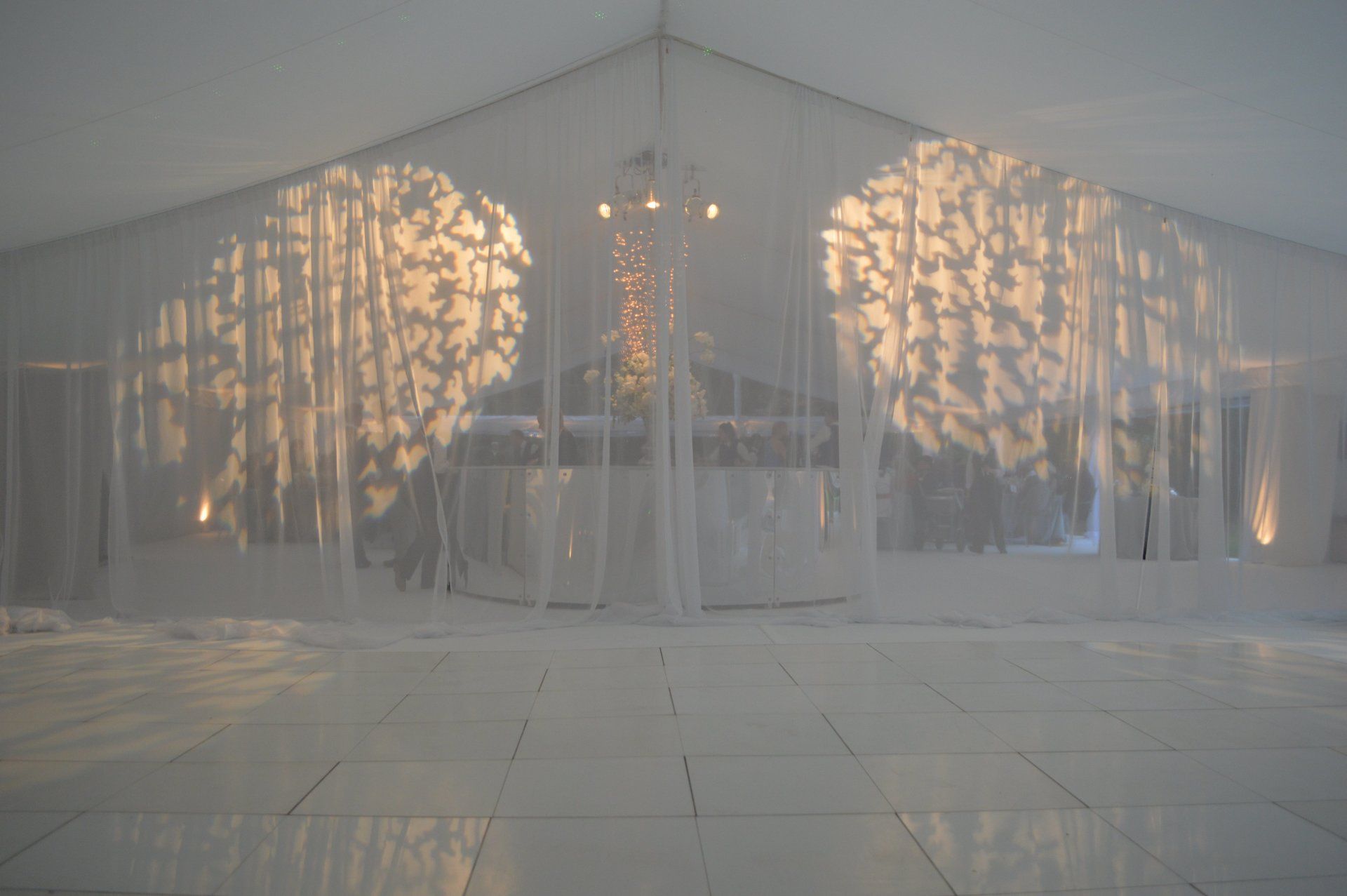 White event tent with sheer drapes and warm lights illuminating a reflective floor