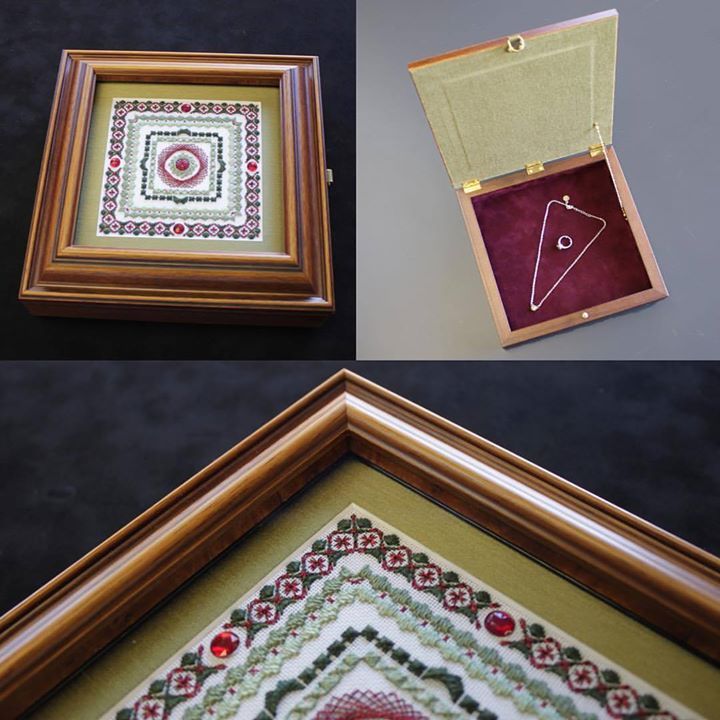 A wooden shadow box featuring an intricate embroidery on its lid and a velvet-lined interior holding a delicate necklace.