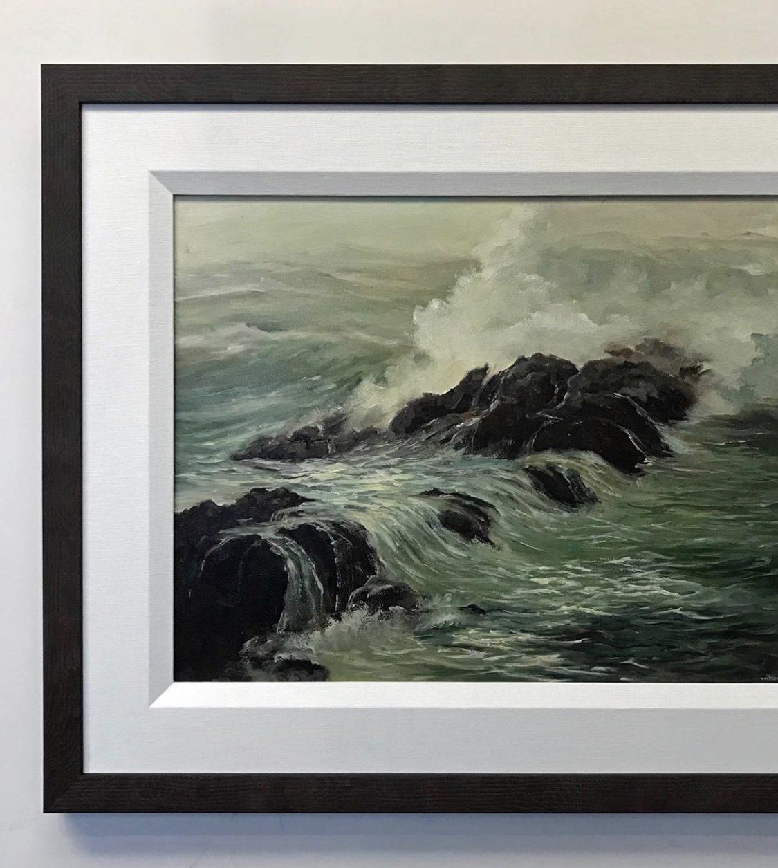 A framed oil painting of ocean waves crashing against dark, jagged rocks in a misty, muted seascape.