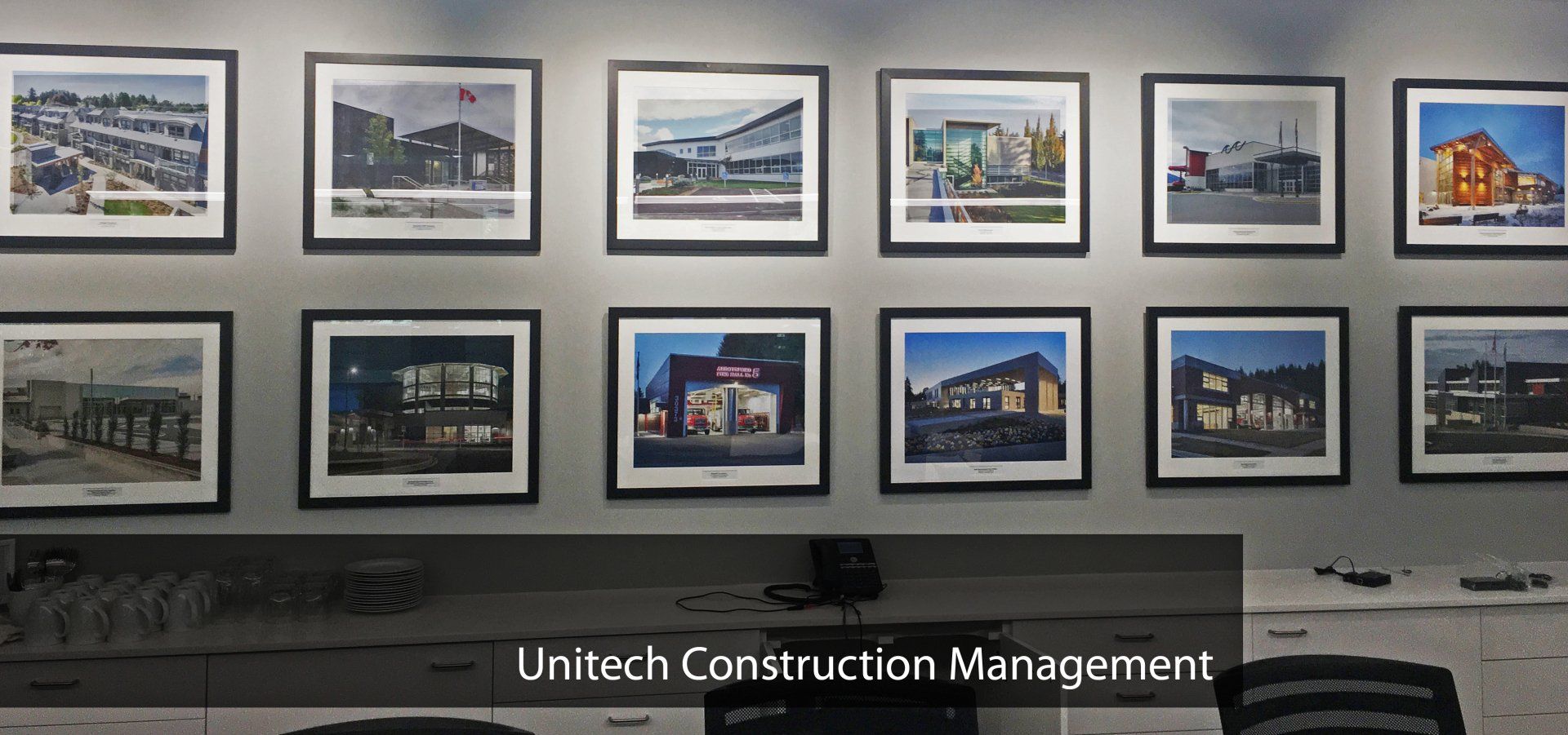 A display of 12 framed photographs of architectural projects mounted on a light gray office wall.