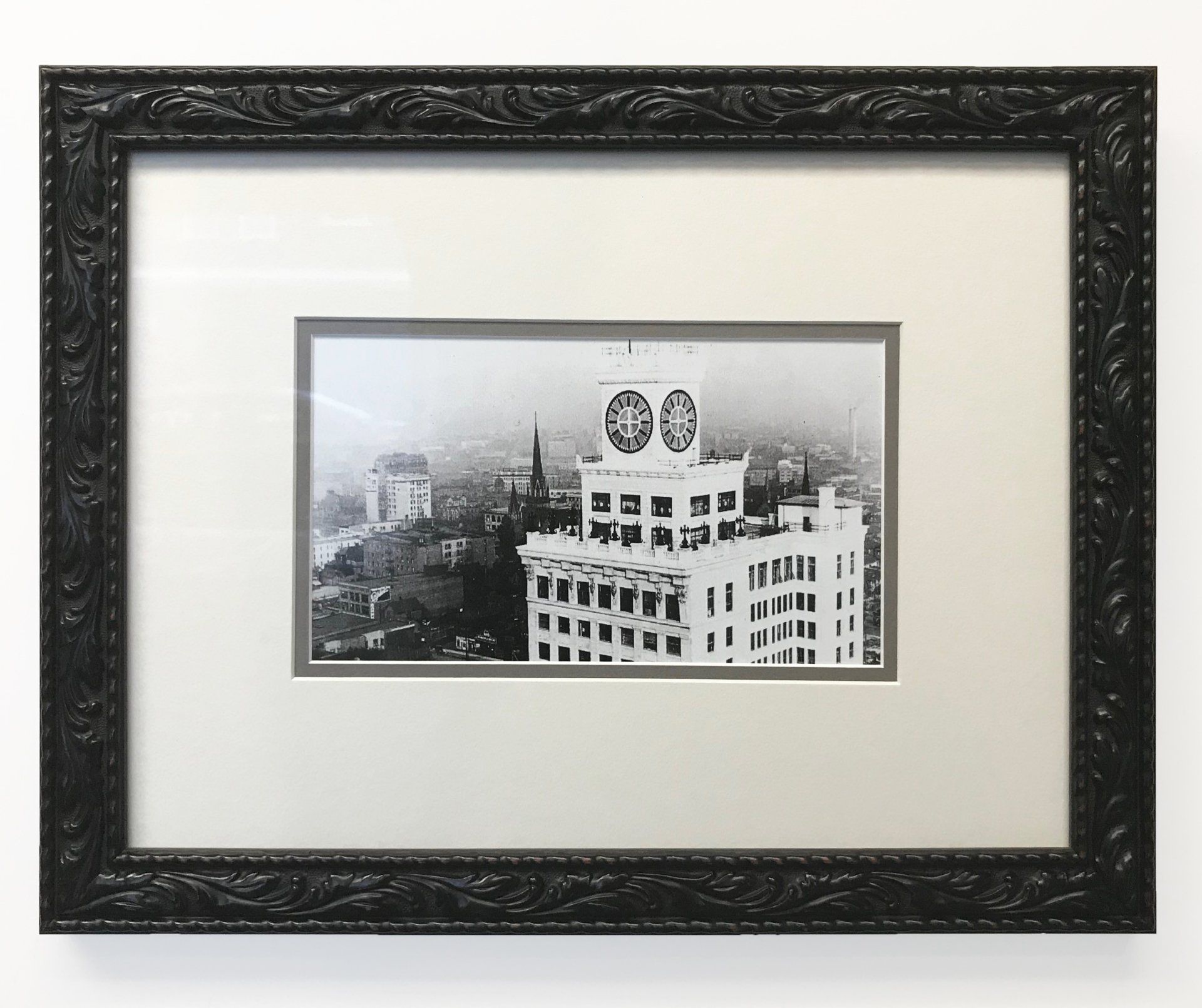 A black-and-white print of a city skyline featuring a tall building with a circular emblem in a dark, ornate frame.