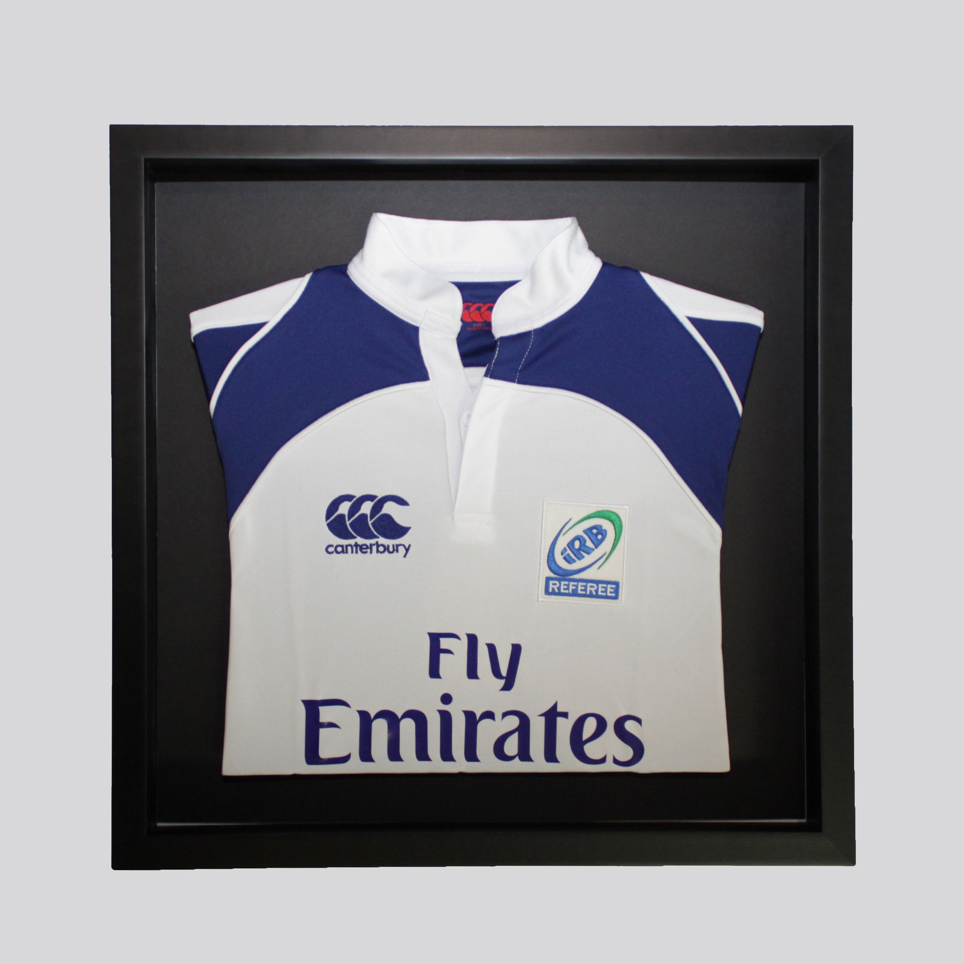 A white and blue rugby jersey with a Canterbury logo, Fly Emirates branding, and an IRB patch displayed in a black frame.