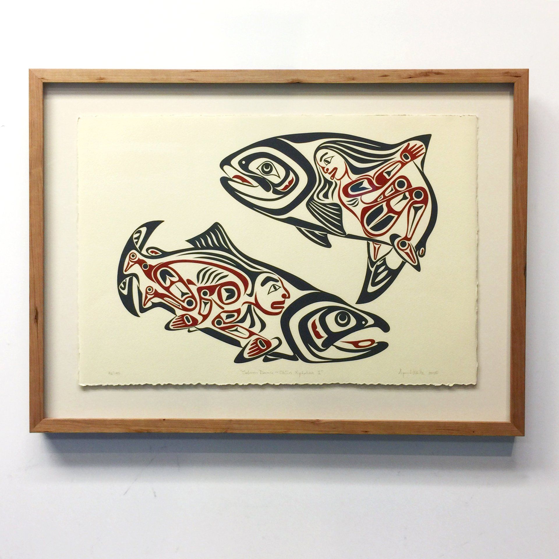 Framed Northwest Coast Indigenous-style print depicting two stylized salmon with human figures integrated into their bodies.
