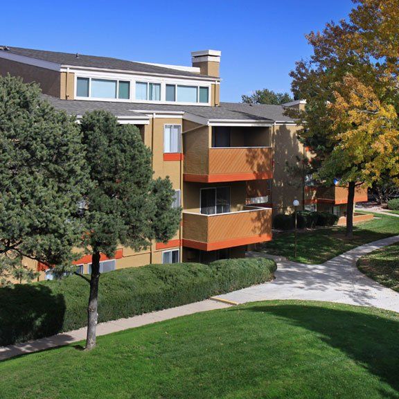 Apartment building with sidewalks going around it, landscaping, grass and trees next to the building