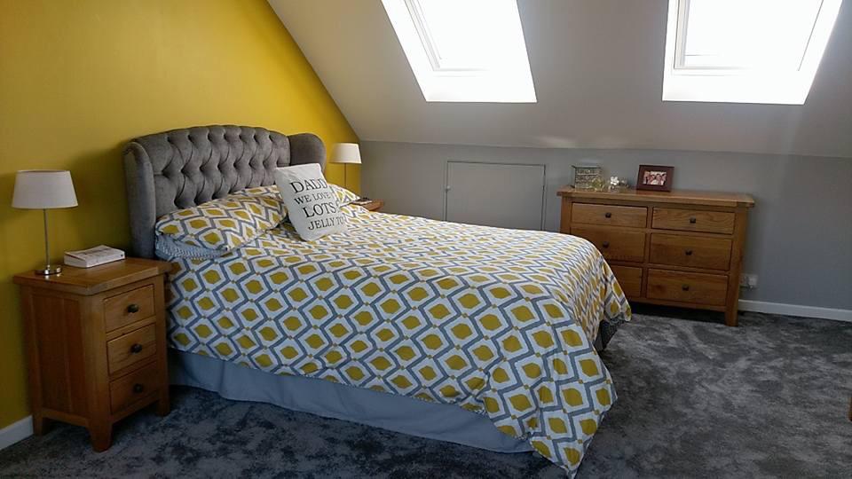 A loft main in bedroom with a bed , dresser , nightstand and yellow walls.