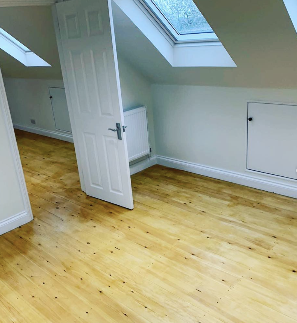 An empty room with a wooden floor and a skylight.