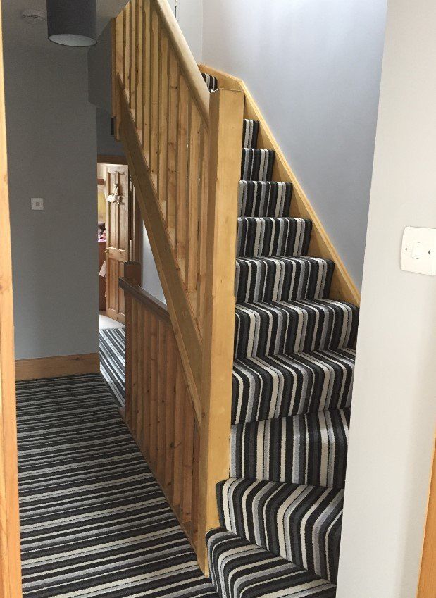 A staircase with a wooden railing and a black and white striped carpet.