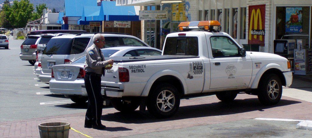 A white pickup truck with flashing lights parked on a street near a person in uniform. Buildings in the background.