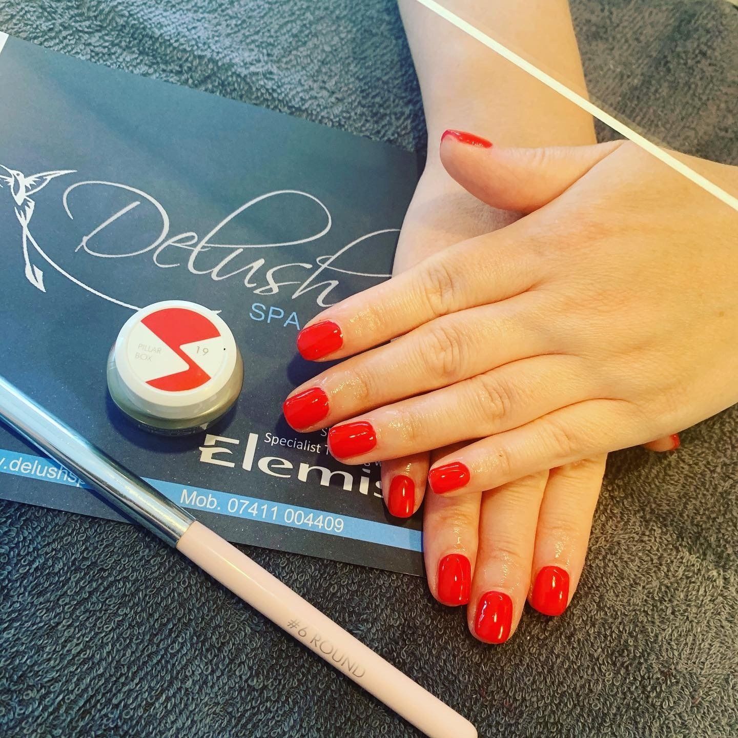 Red-manicured hand resting on a beauty booklet beside nail tools on a textured surface.