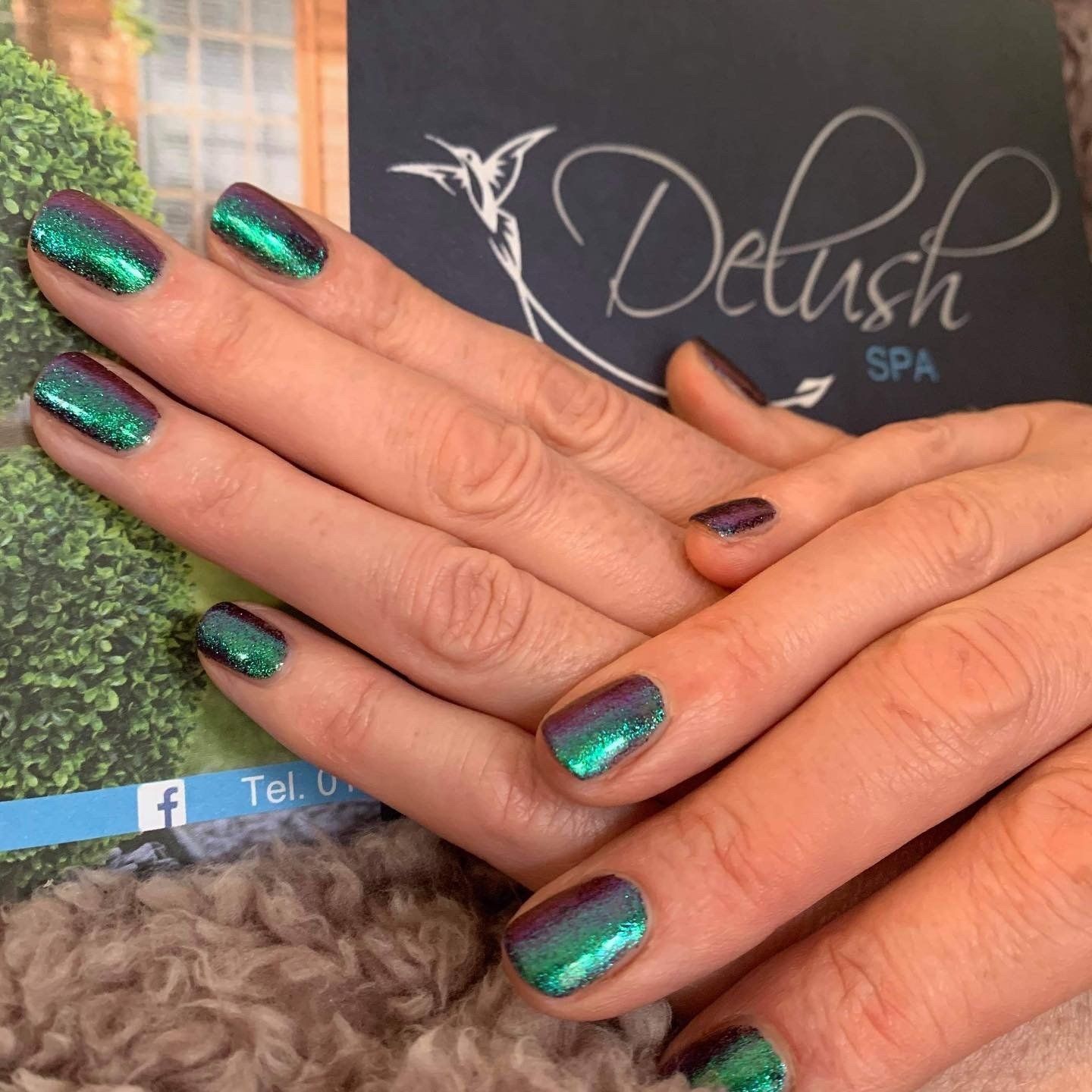 Hands with teal iridescent manicure resting on a Delush Spa card background