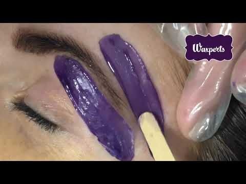 Purple wax strips on a person’s eyebrow during a waxing procedure