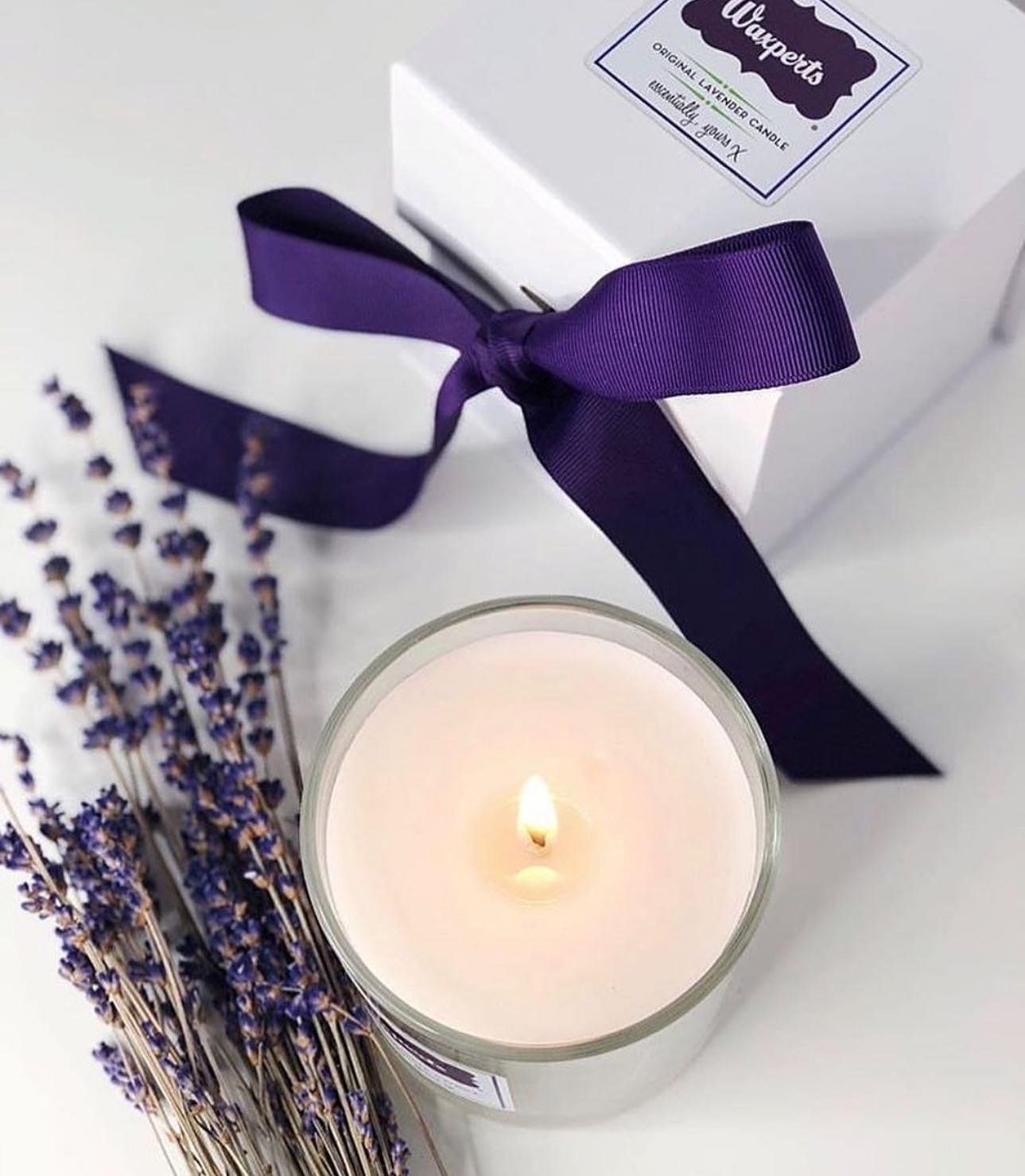 Lavender-scented candle with purple ribbon and dried lavender sprigs on a white box