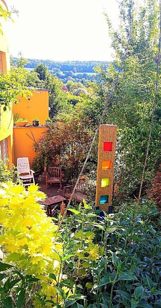 Ein Garten mit einer Holzskulptur in der Mitte und einem gelben Gebäude im Hintergrund.