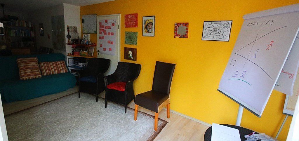 Ein Wohnzimmer mit einer gelben Wand und Stühlen und einer weißen Tafel