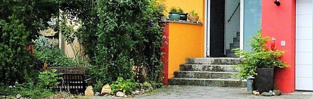 Ein gelbes Haus mit einem roten Garagentor und Treppen