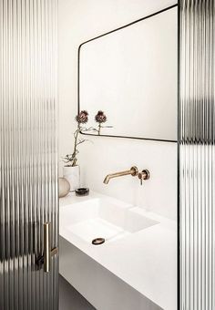 Minimal white bathroom vanity with brass faucet, round mirror, and ribbed glass partition