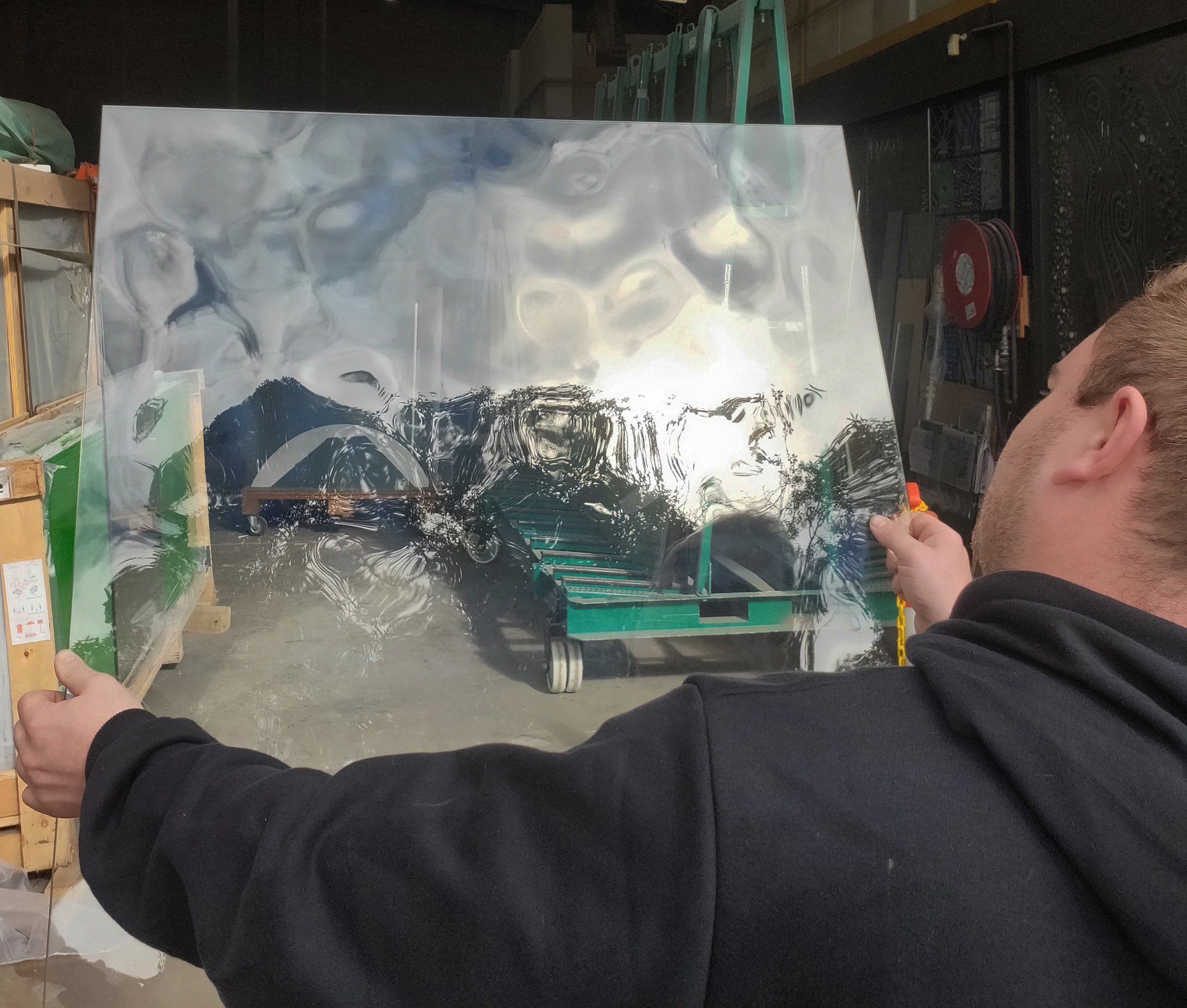 Person holding up a reflective sheet in a workshop, reflecting a mountain landscape.