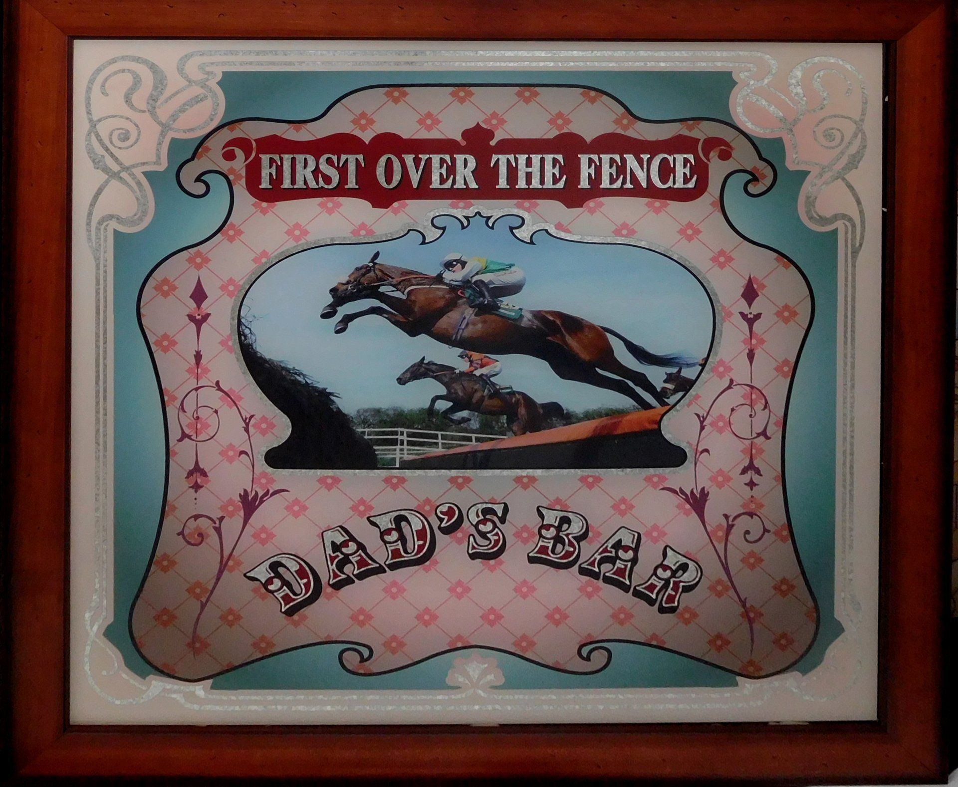 Framed sign with a galloping horse and the words “First Over the Fence” and “Bad’s Bar.”