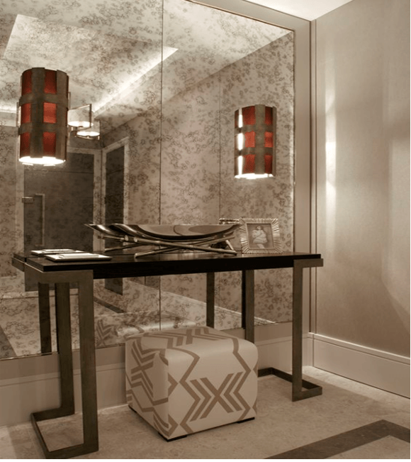 Modern vanity table with black legs, mirror, and patterned ottoman in a beige bathroom