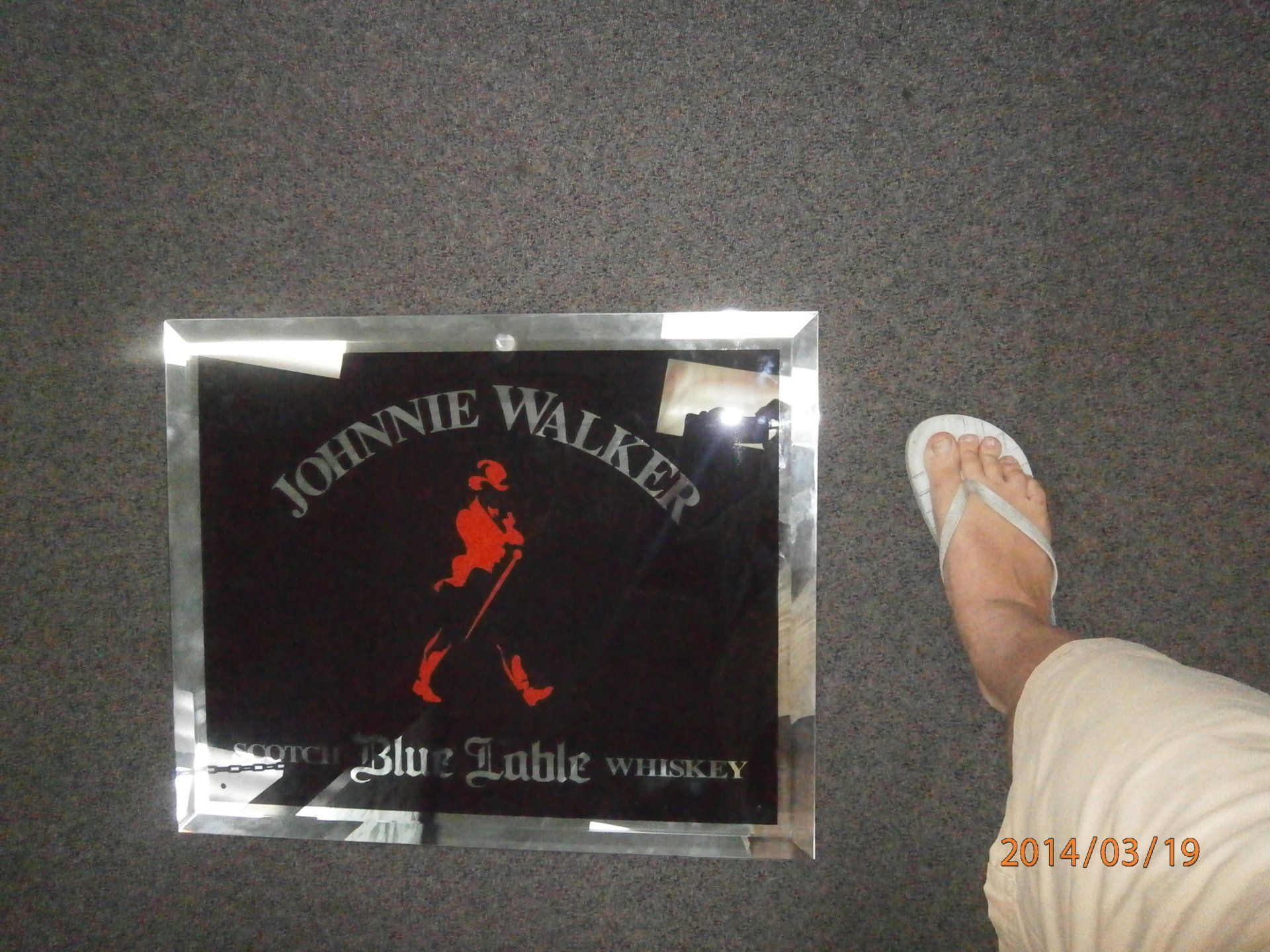 Johnnie Walker logo on a black sign beside a foot in a white sandal on gray pavement