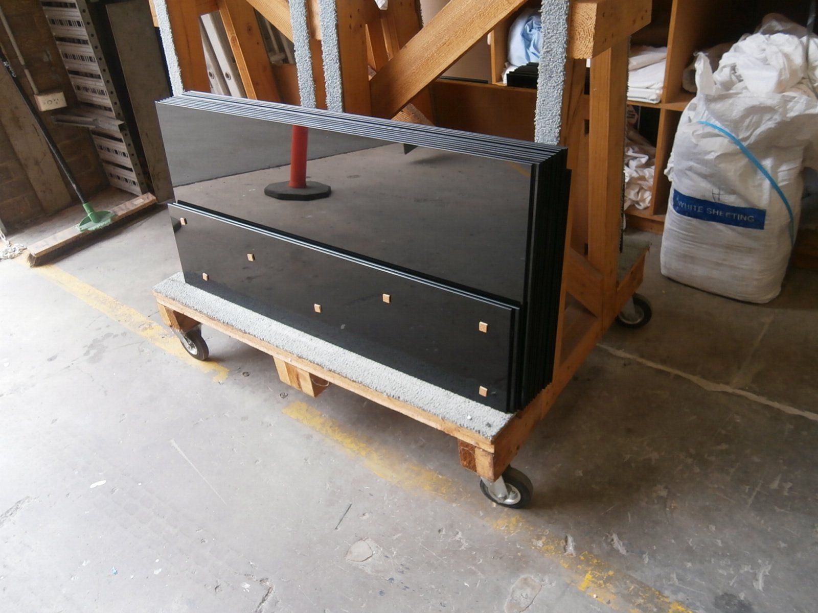 Black metal cart on a wooden dolly in a workshop, with a striped barrier on top.