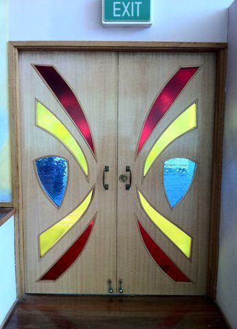 Wooden double doors with colorful red, yellow, and blue glass accents beneath an exit sign