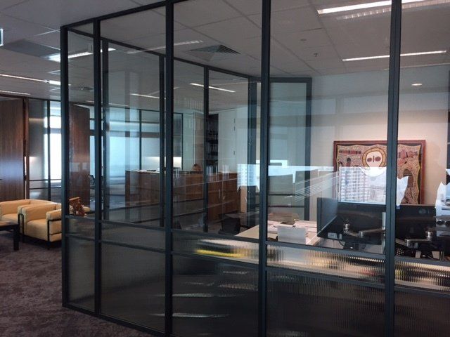 Modern office with glass-walled cubicles and desks under bright ceiling lights