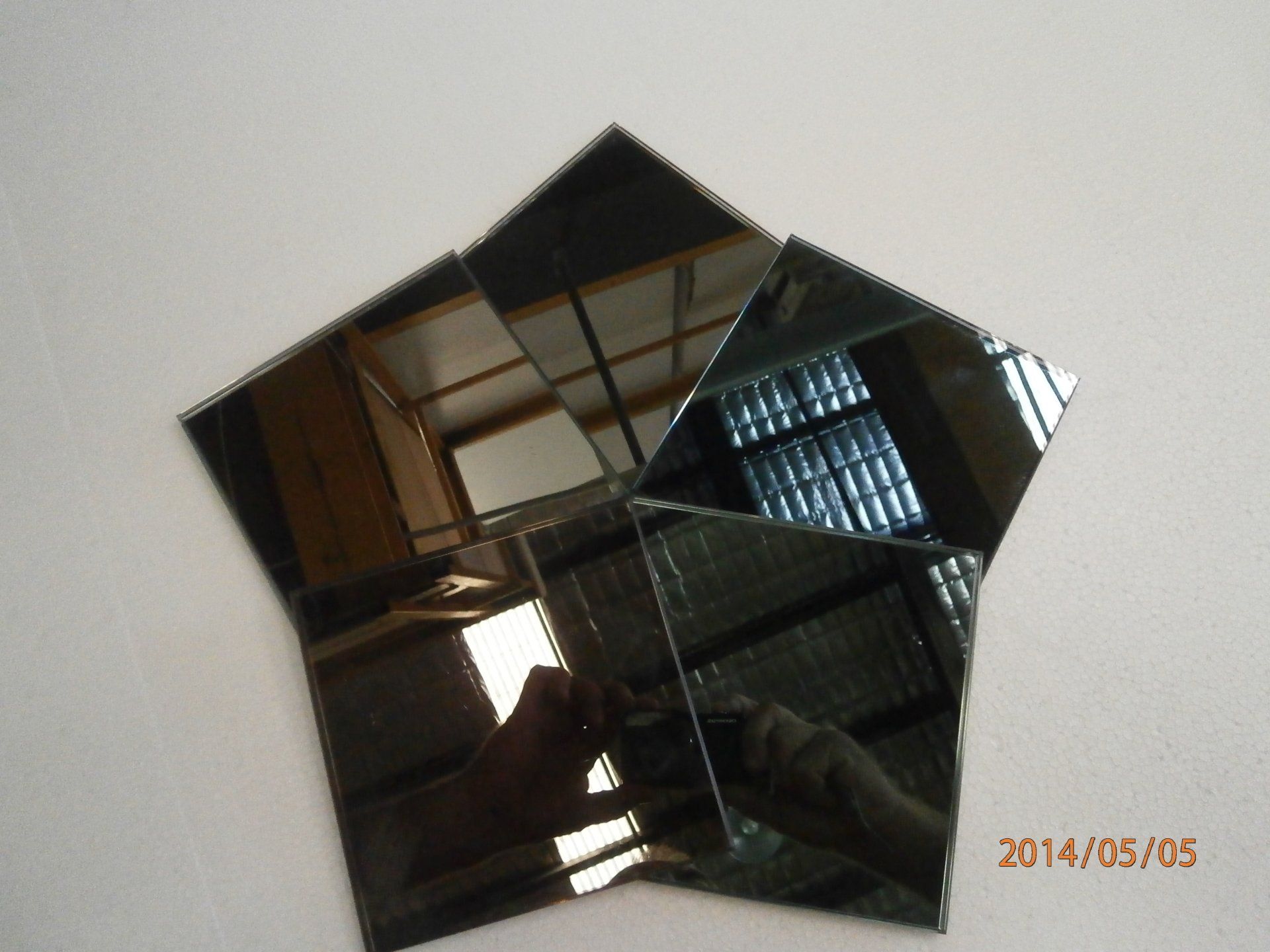 Diamond-shaped mirrored wall art reflecting a room interior and a person holding the camera.