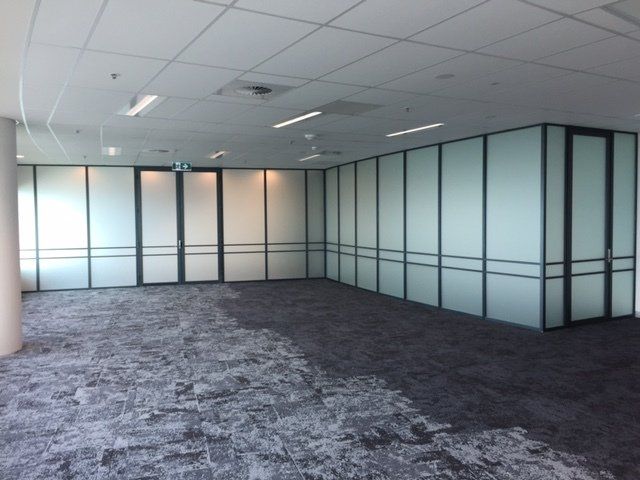 Empty office space with gray carpet, frosted glass walls, and ceiling lights