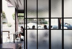 Modern cafe interior with a person seated by a window and parked cars visible outside