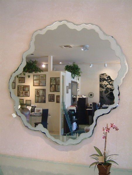 Scalloped wall mirror reflecting a salon with framed art, plants, and a pink orchid in the foreground