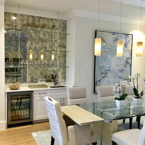 Modern dining area with glass table, white chairs, marble wall, and pendant lights beside a small bar nook