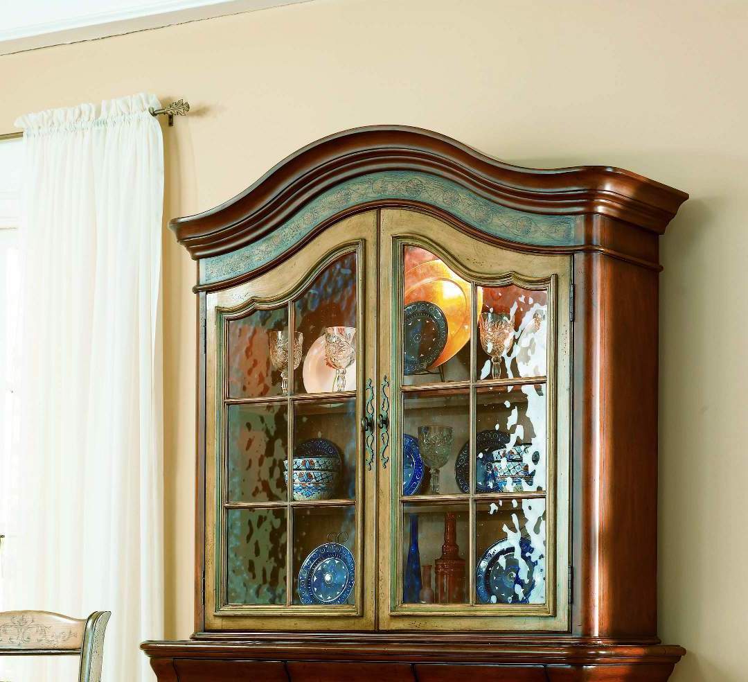 Wooden glass-front cabinet with blue dishes and decor in a bright room beside a white curtain