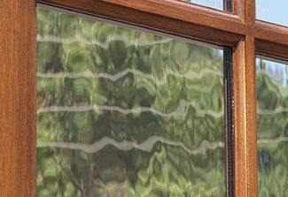 Wooden-framed window with wavy, frosted glass showing blurred greenery outside