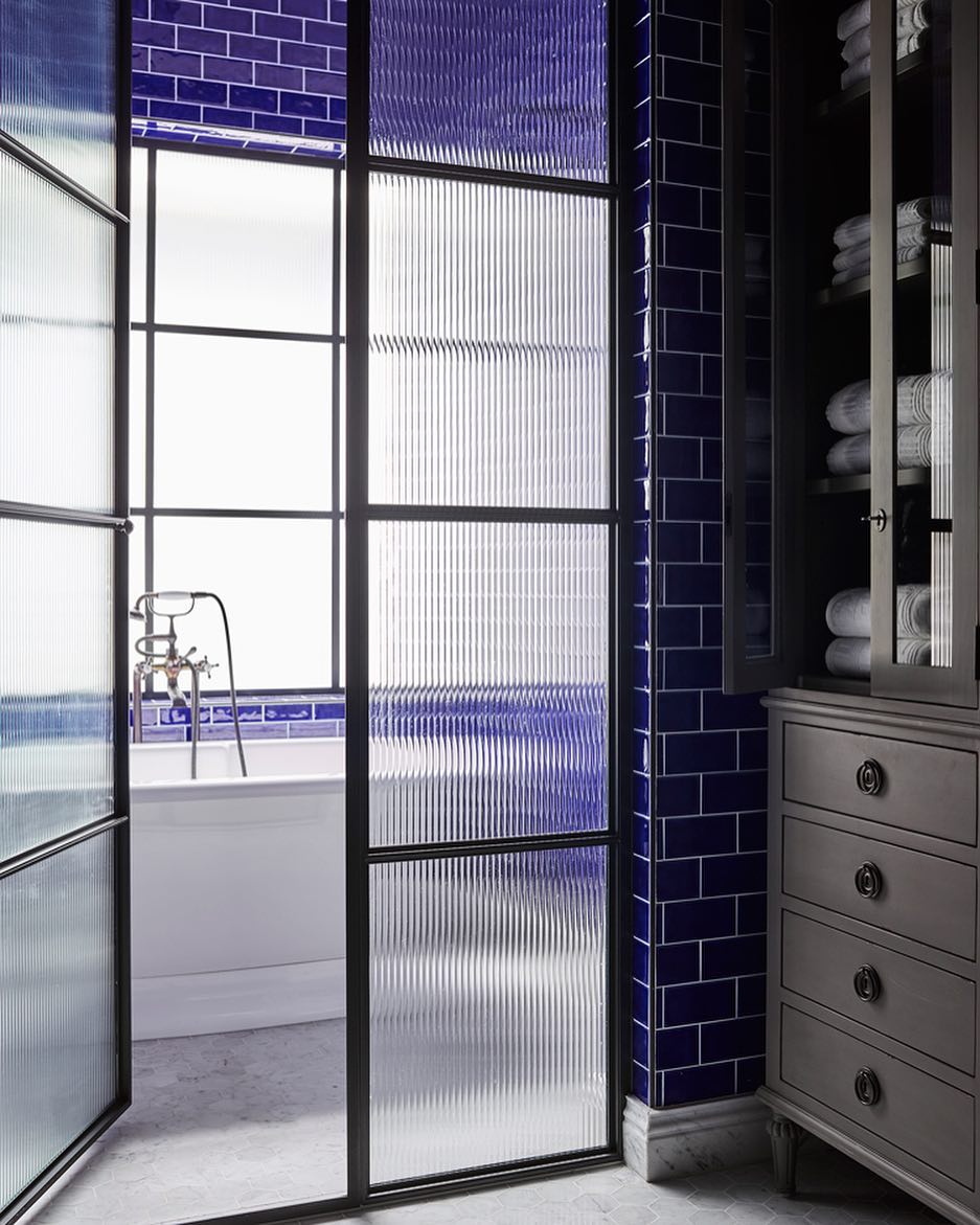Modern bathroom with frosted glass shower, blue tile, white tub, and a mirrored vanity cabinet
