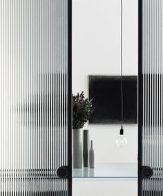 Modern interior with ribbed glass doors, a wall mirror, hanging bulb, and small decor on a shelf.