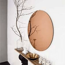Stylish wall mirror above a console table with white decor, bare branches, and brass bowl