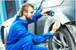 A man in blue overalls is painting a car.
