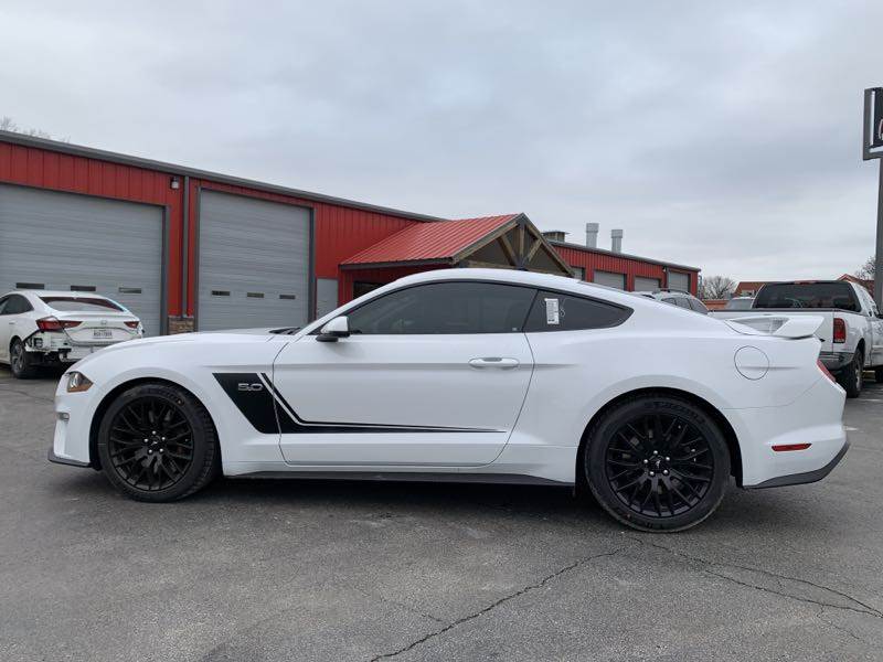 A white ford mustang is parked in front of a garage.