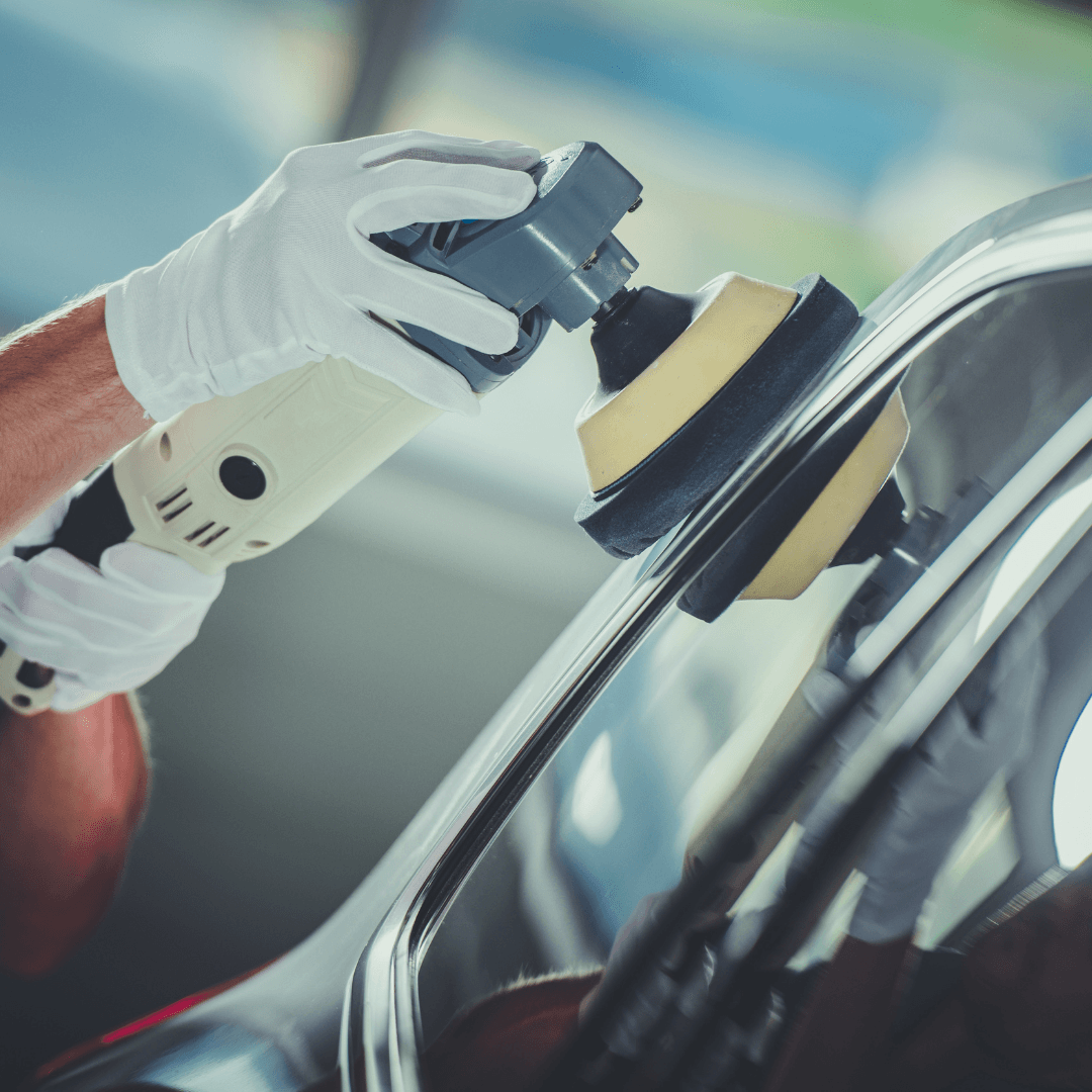 Person wearing gloves polishing car window with electric buffer.