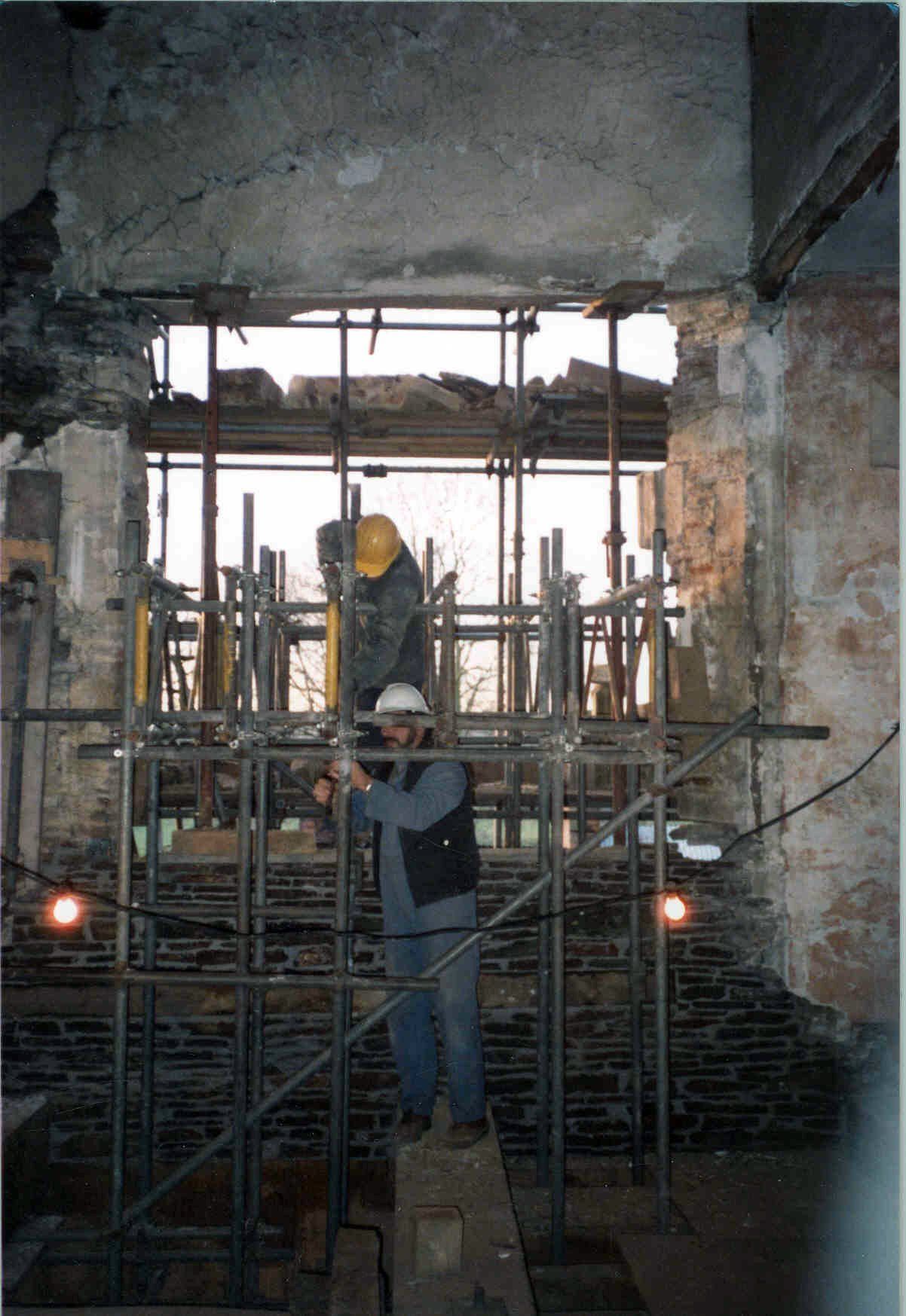 A man wearing a hard hat is working on scaffolding at Acton Court