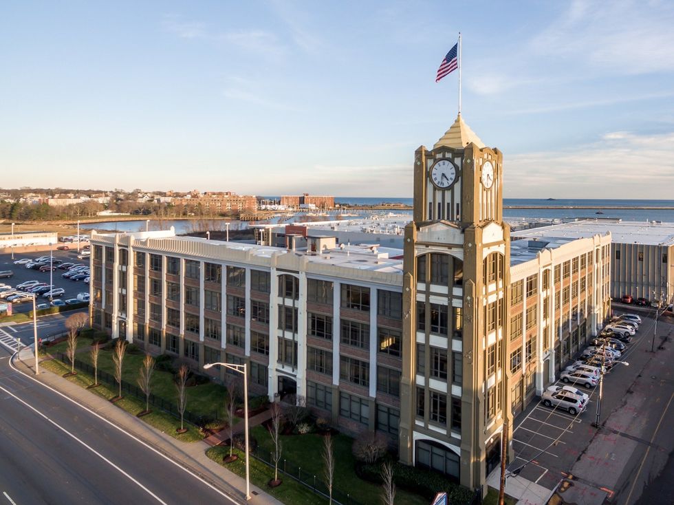 An aerial view of a large building with a clock tower and a flag on top.