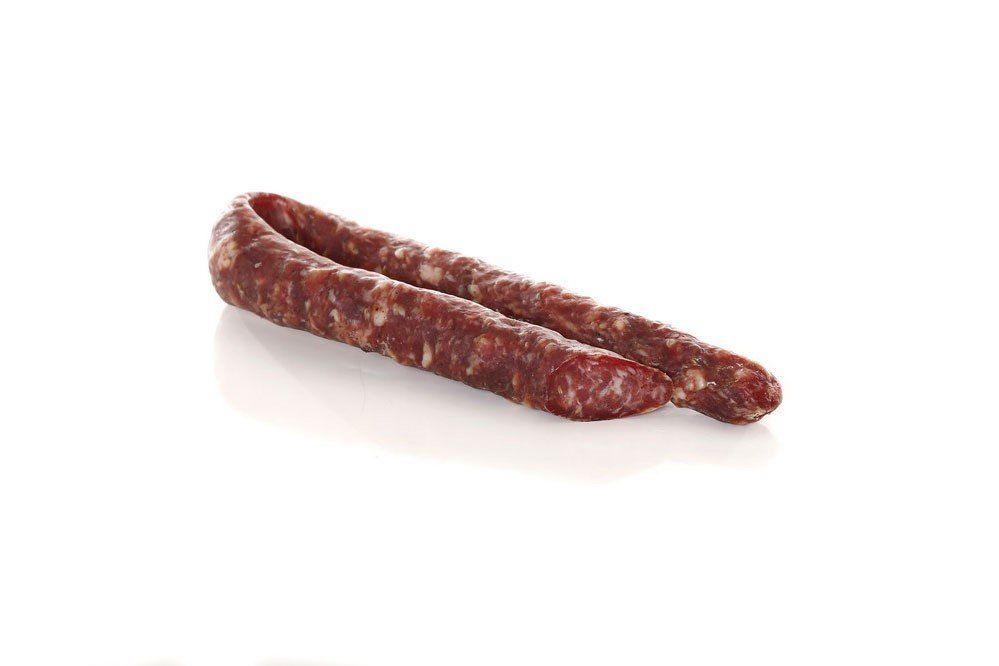 Un pezzo di salsiccia è appoggiato su una superficie bianca.