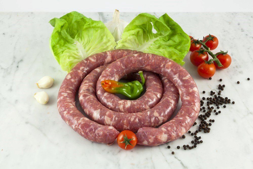 Una salsiccia è appoggiata su un tavolo accanto a lattuga e pomodori.